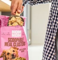 A close up of someone scooping a cupful of Nom Nom scoopable meal clusters out of its packaging